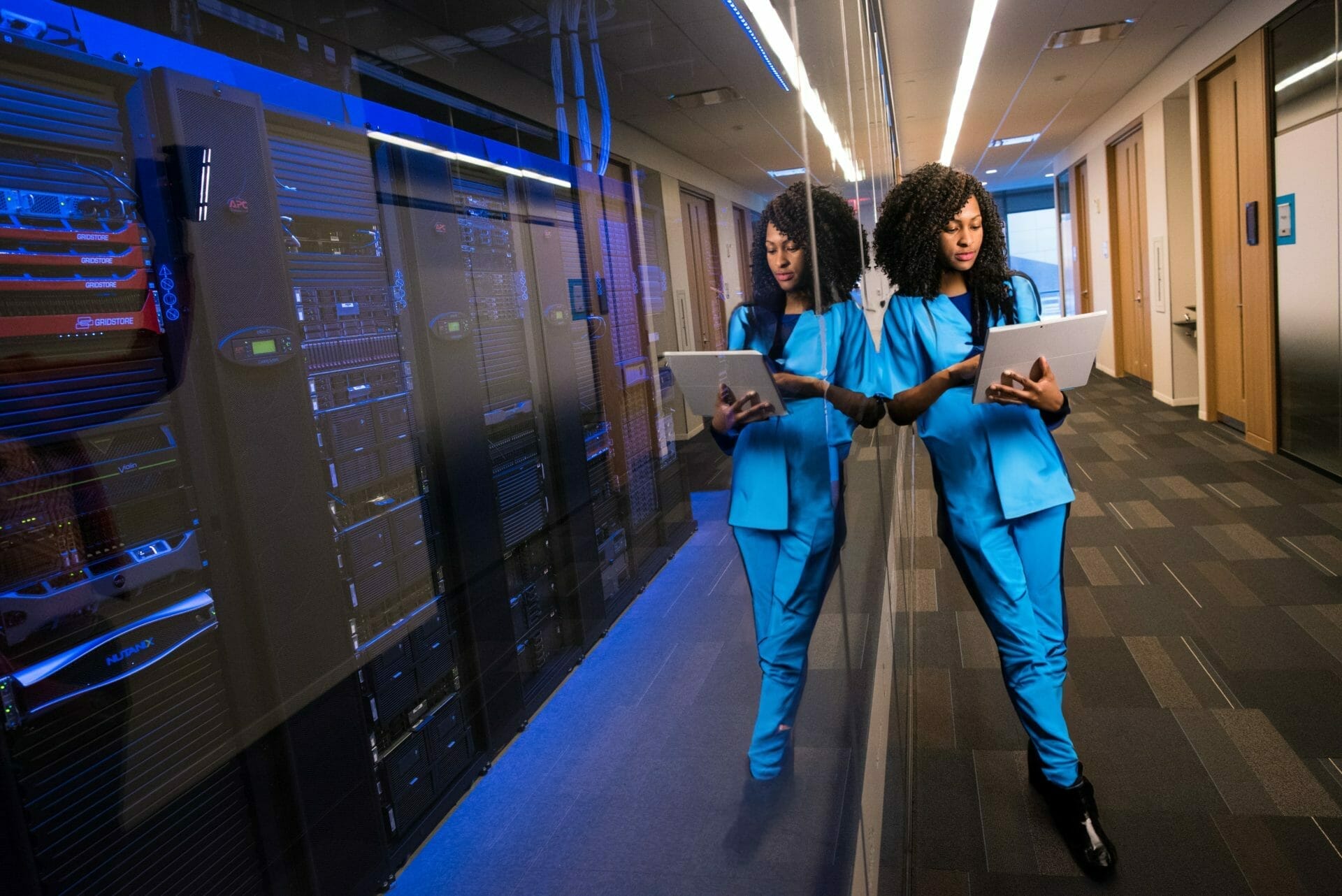 IT technician in scrubs using a tablet in a data center hallway